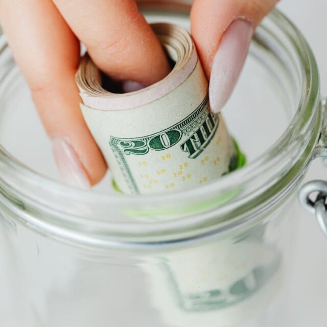 Savings Calculators_Hand placing rolled US dollars into a glass jar, representing savings and financial planning.