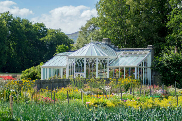 2026_05_Monthly-Market-Commentary_Spring-Garden-image-with-greenhouse-and-lots-of-flowers_
